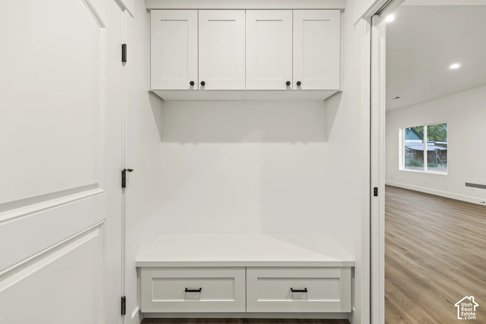 Built-in mudroom bench with two storage drawers, upper shaker-style cabinetry with matte black hardware, and wood-finish flooring