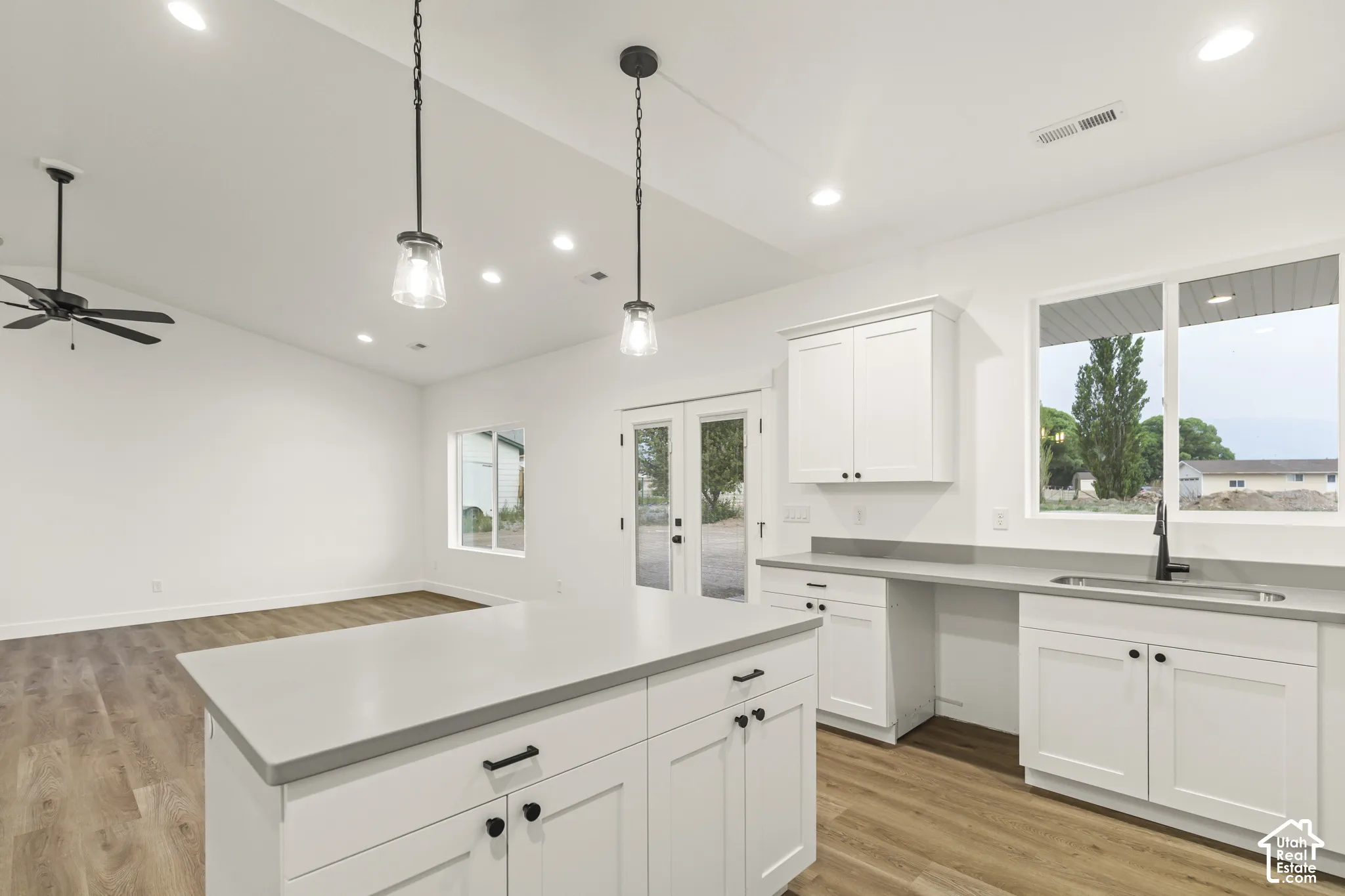 Open-concept kitchen featuring an island with white shaker cabinetry, light-toned countertops, and two pendant lights