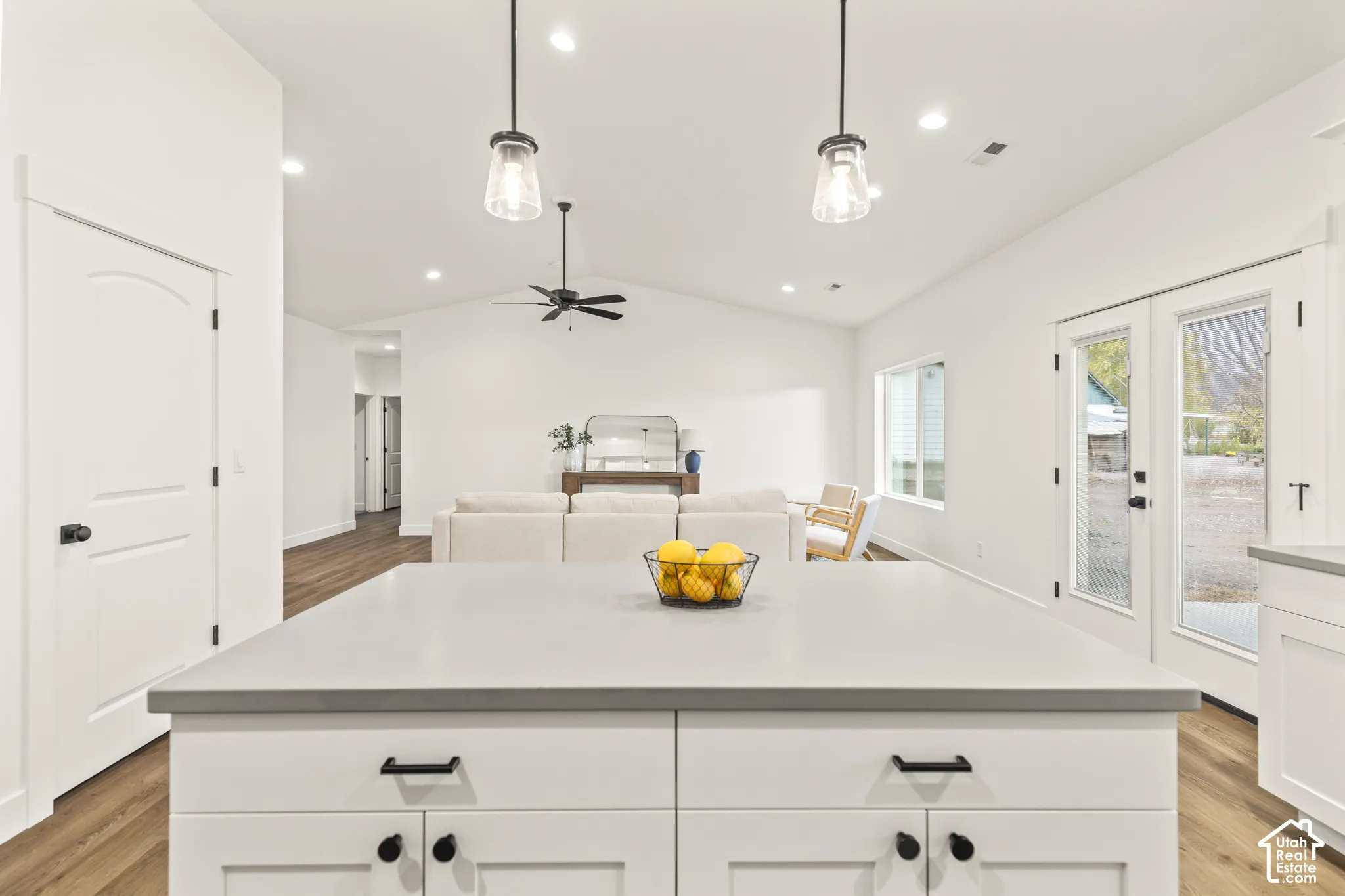 Kitchen island with solid surface countertop and matte black hardware, vaulted ceilings, recessed lighting, dual glass-paned exterior doors, and wood-finish flooring
