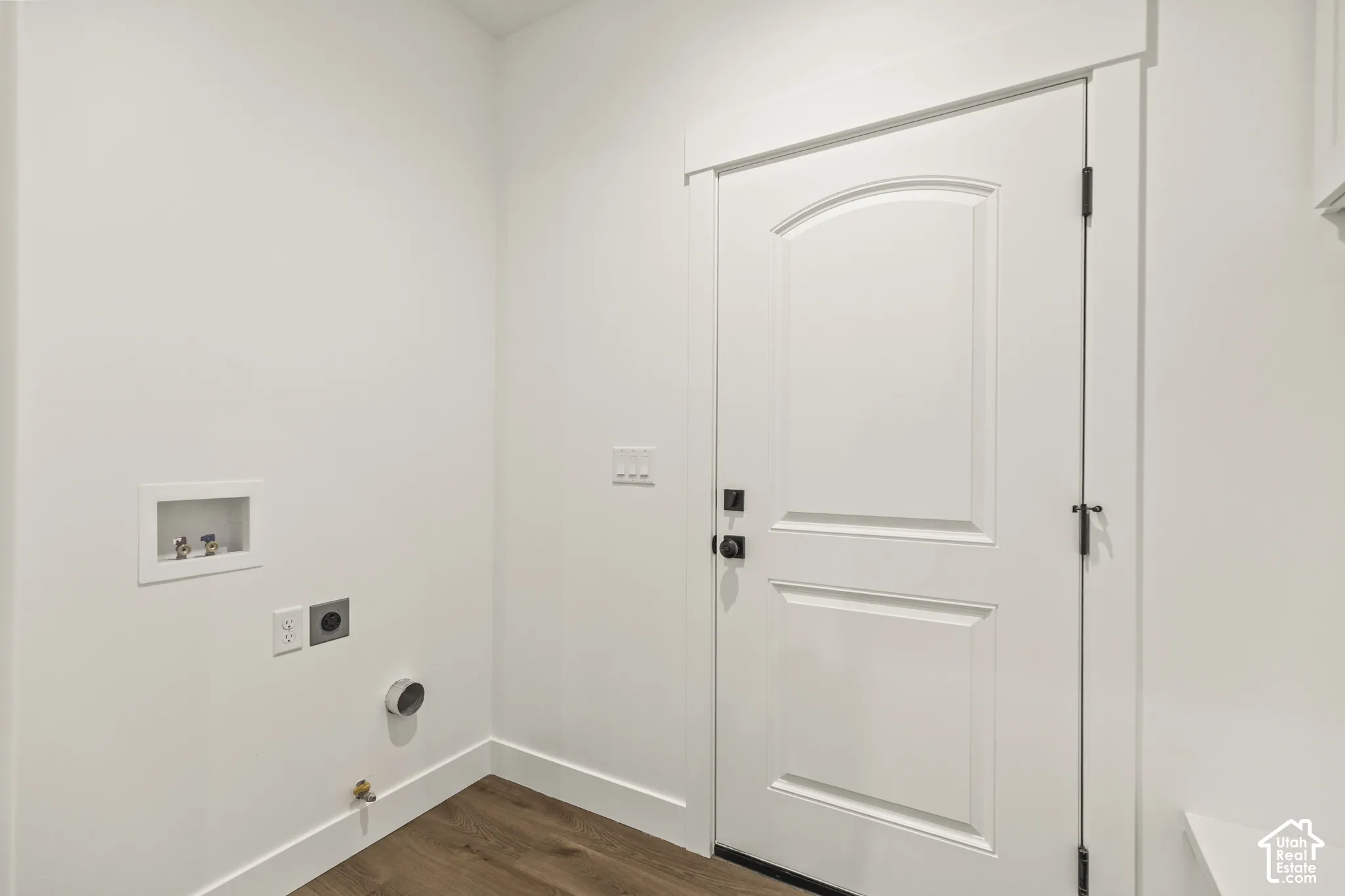 Dedicated utility area featuring wood-finish flooring, white walls, and a paneled door with dark hardware