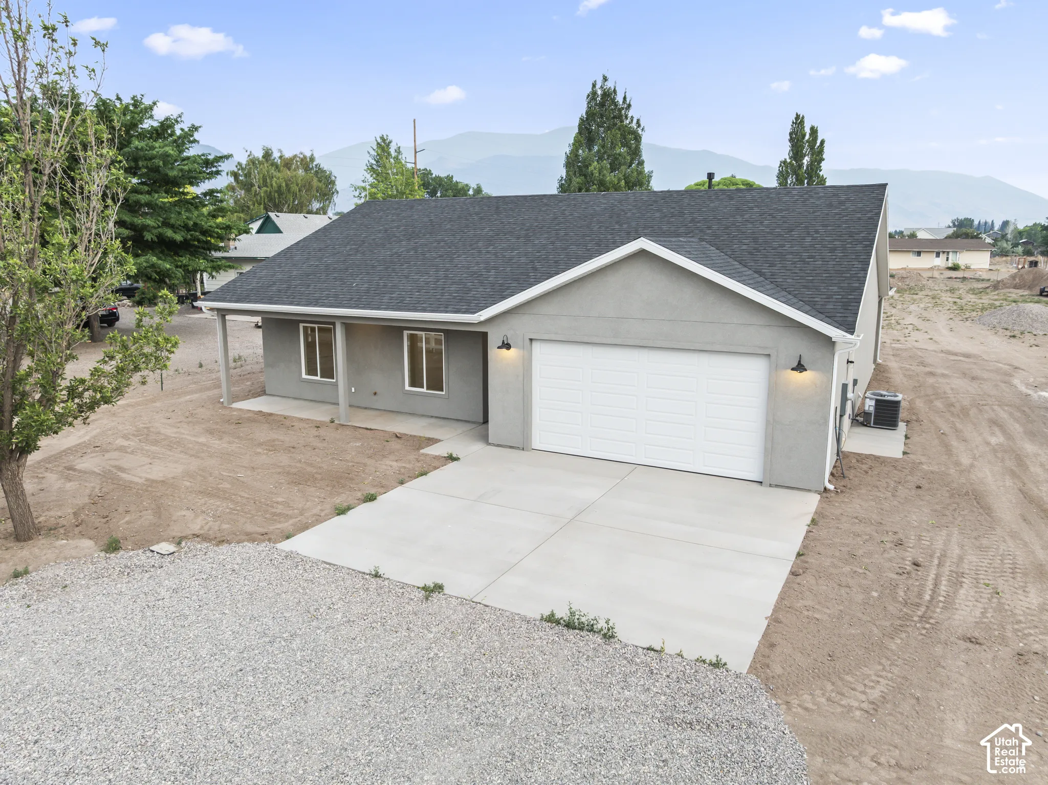 Contemporary stucco exterior featuring a two-car garage, covered entry, concrete driveway, dark shingle roof, and exterior lighting fixtures