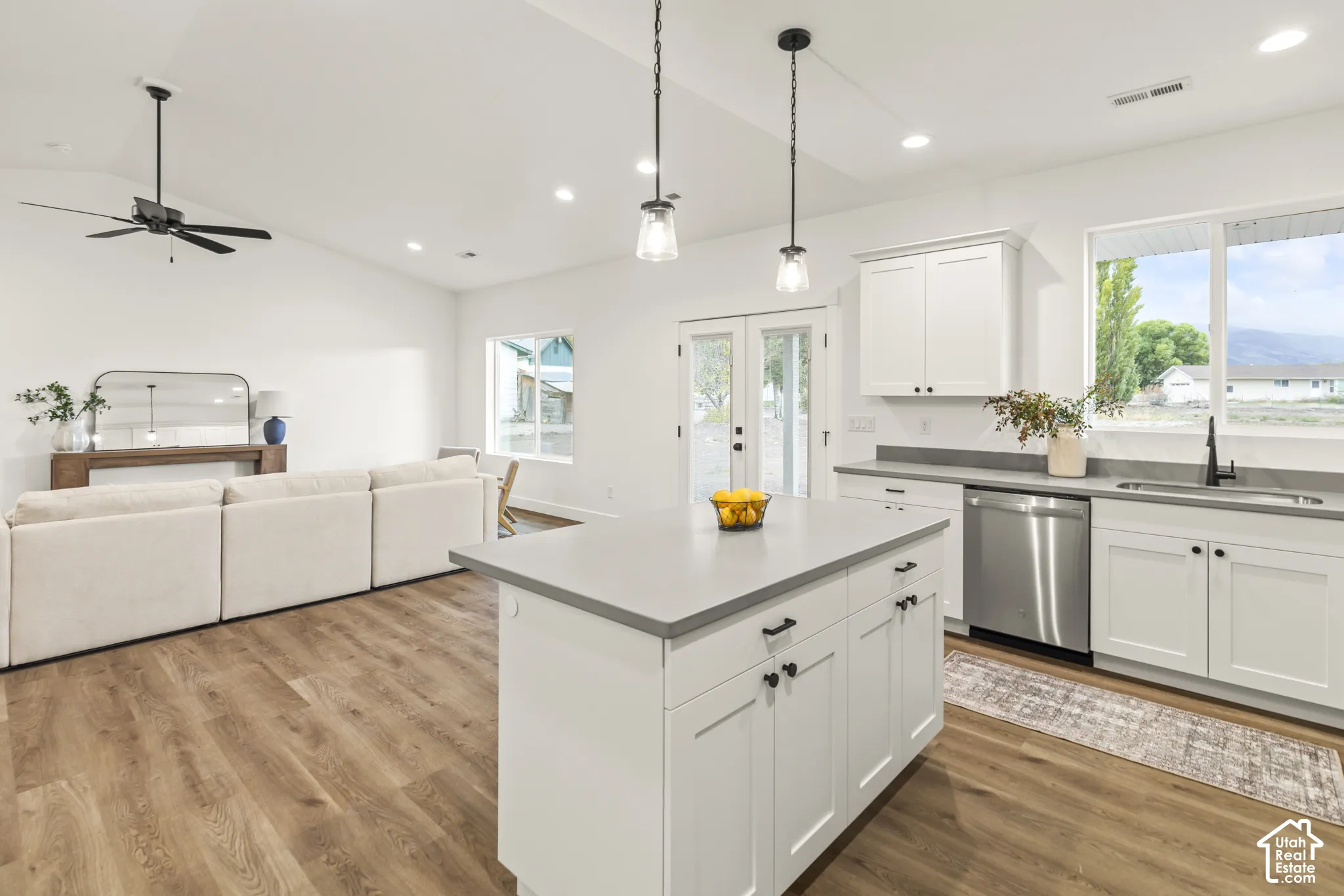 Kitchen featuring white cabinetry, a center island with a stone-finish countertop, stainless steel dishwasher, pendant lighting, and wood-finish flooring