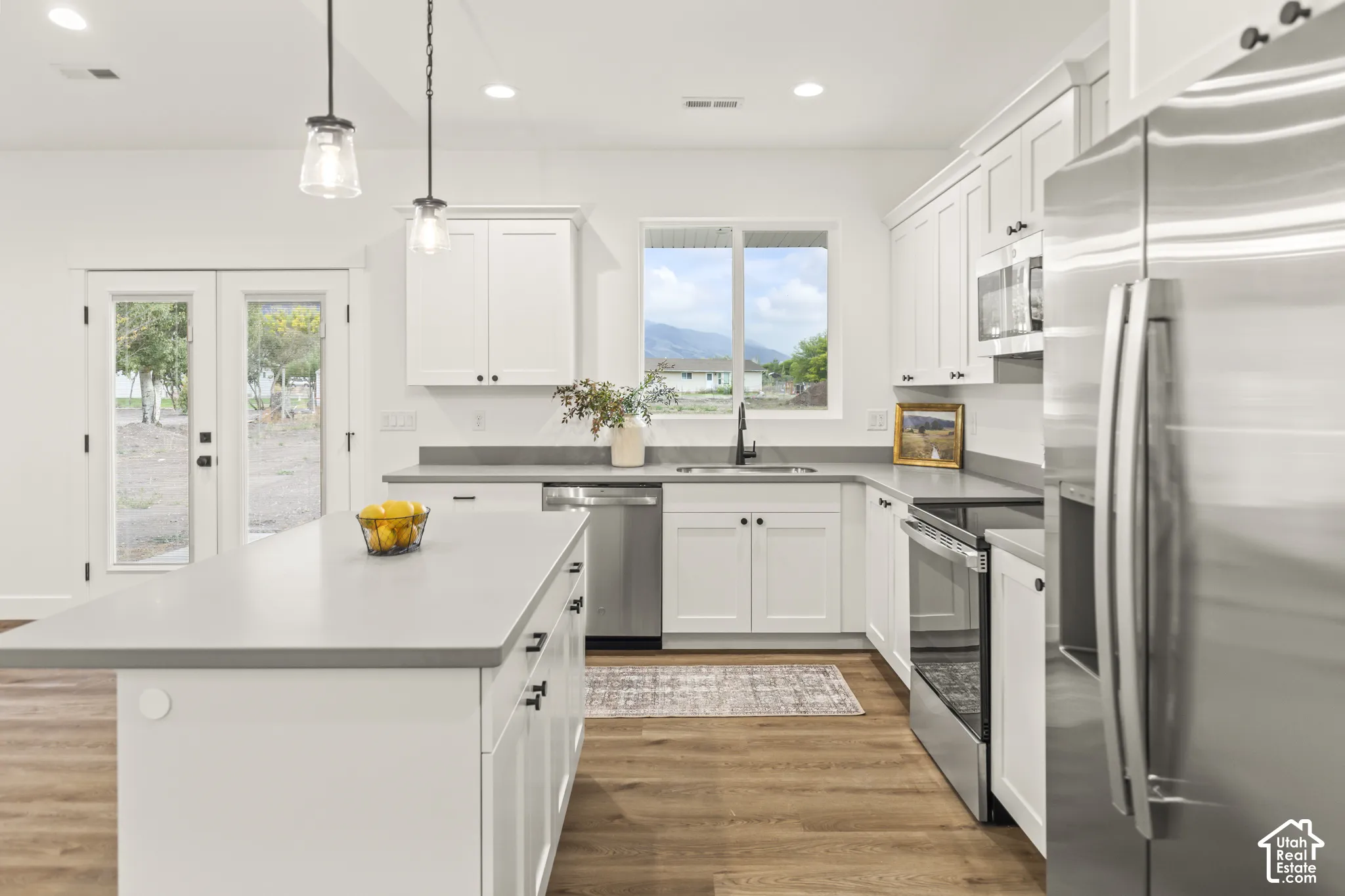 Kitchen featuring white cabinetry, solid-surface countertops, wood-finish flooring, stainless steel appliances, and a central island