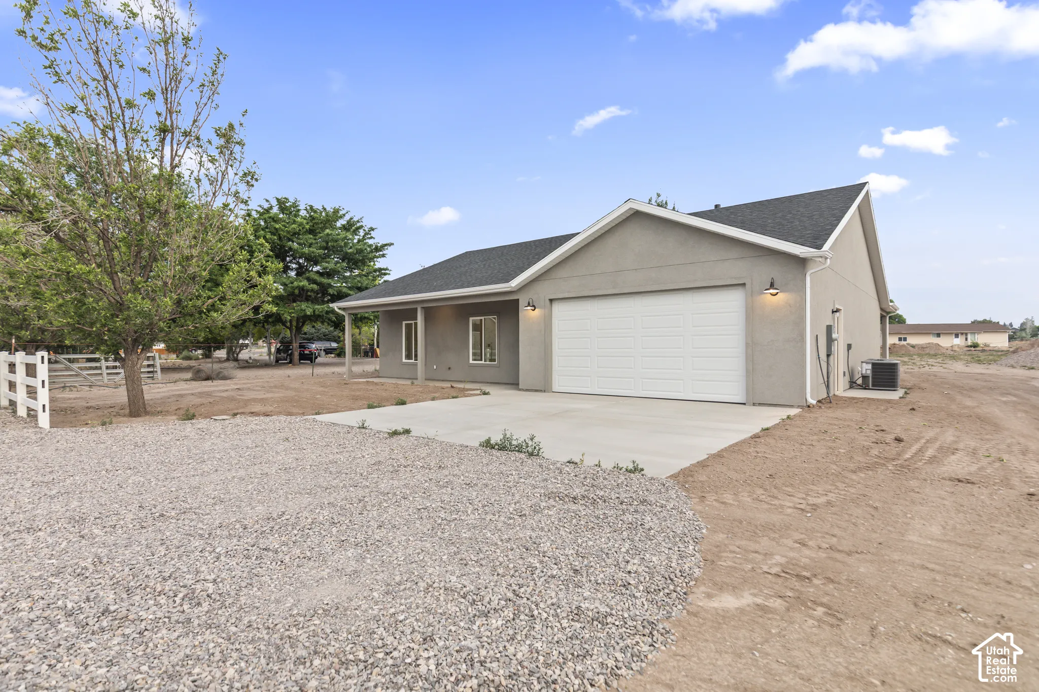 Exterior showcasing a stucco finish, attached garage with a panel door, concrete driveway, and black asphalt shingles