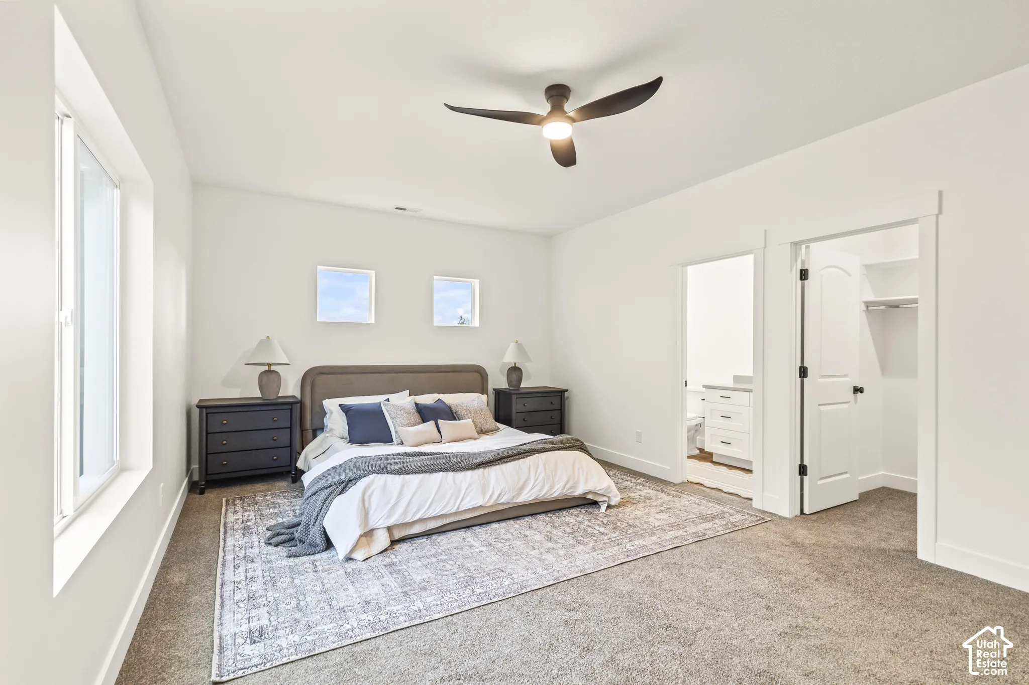 Neutral-toned carpeting, matte black ceiling fan with integrated lighting, dual square windows, and an arched-top closet door