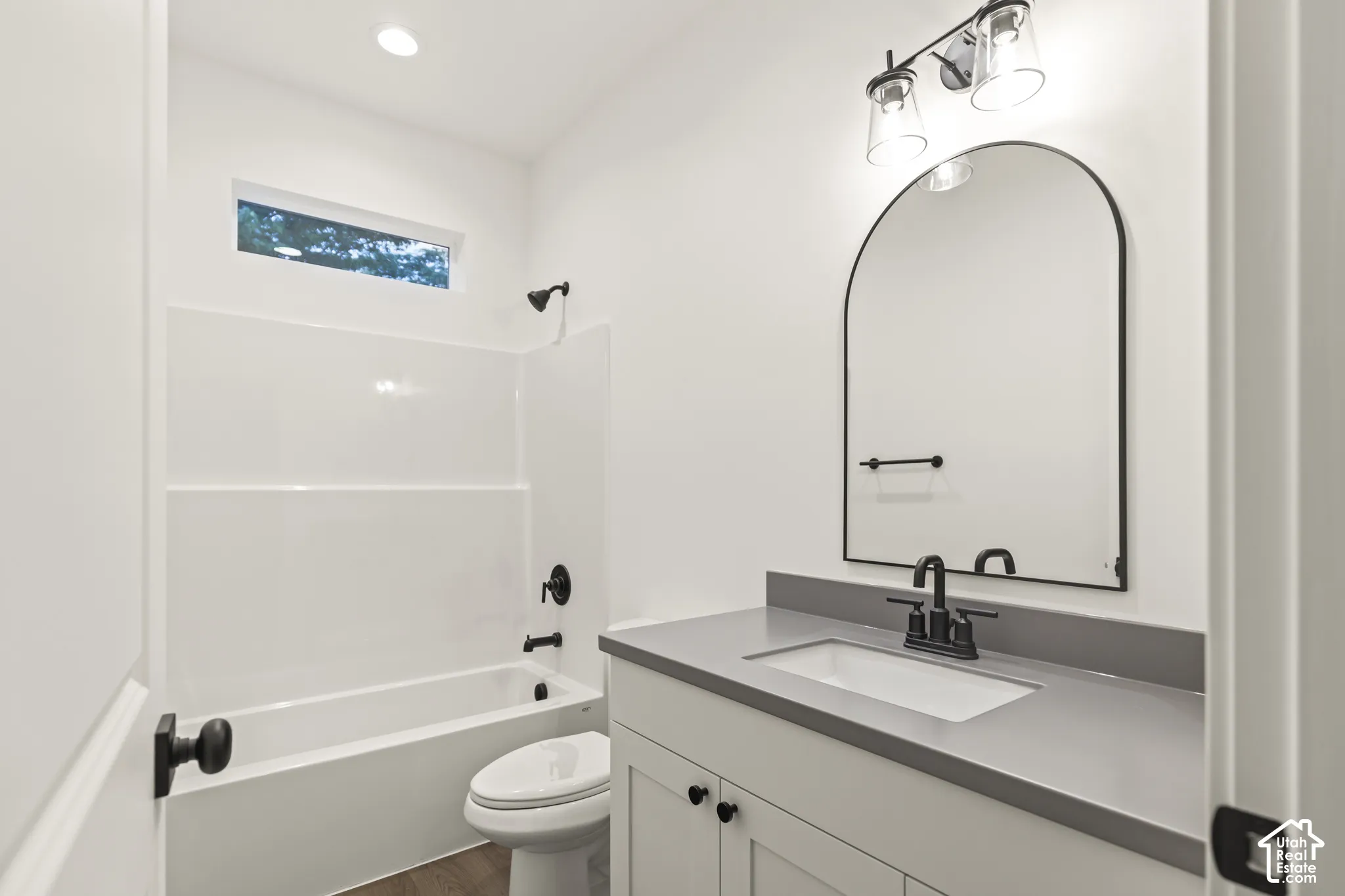 Bathroom featuring a white vanity with a gray countertop, an arched black-framed mirror, a tub-shower combination with a white surround, and dark bronze fixtures