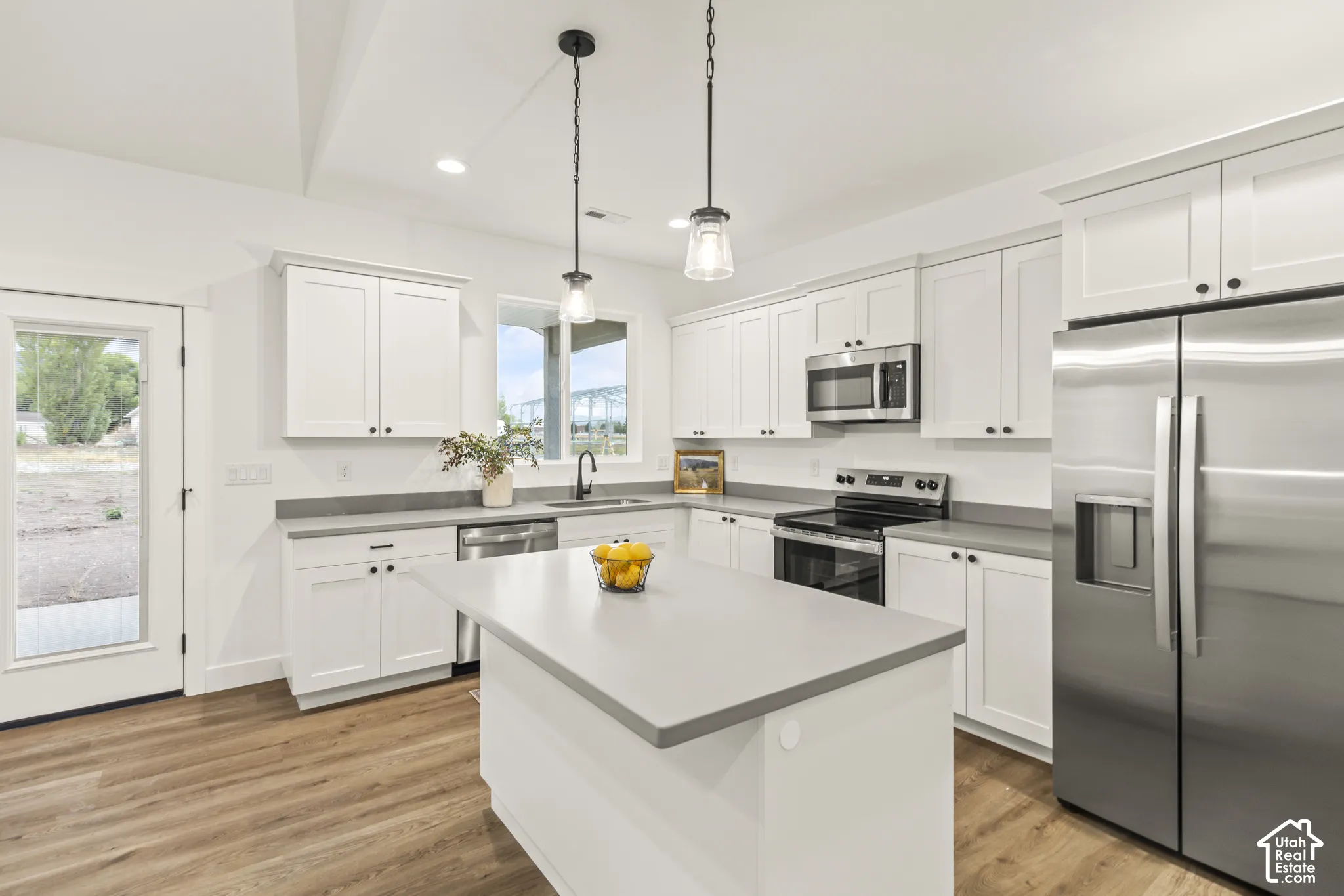 Kitchen featuring white shaker-style cabinetry, solid-surface countertops, wood-finish flooring, a central island, and stainless steel appliances