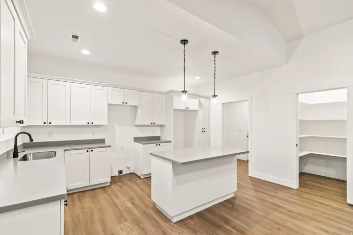Kitchen featuring white shaker cabinetry, an island with countertop, stainless steel sink with a matte black faucet, wood-finish flooring, and a walk-in pantry with shelving