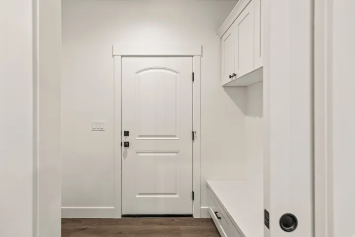 Entryway featuring wood-finish flooring, white paneled door with dark hardware, built-in bench, and overhead cabinetry
