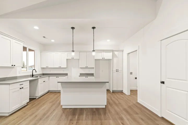 Modern kitchen featuring white shaker cabinetry, an island with countertop, wood-finish flooring, recessed lighting, and pendant fixtures