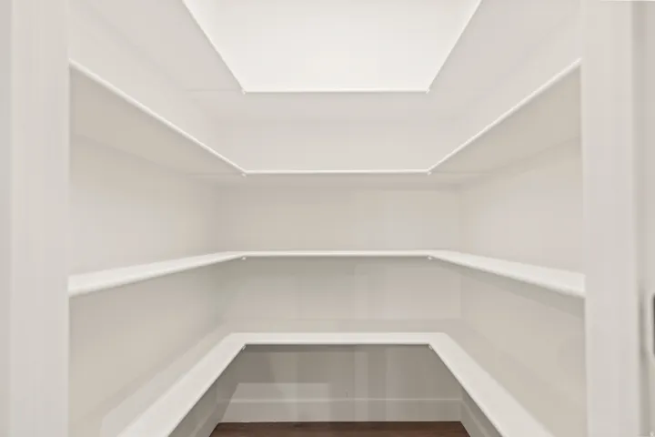 Walk-in pantry with extensive built-in shelving, bright white walls, and wood-finish flooring