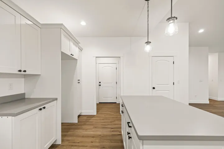 Kitchen featuring a central island with light-toned countertops, white cabinetry with dark hardware, and wood-finish flooring