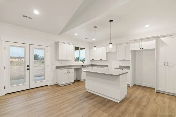 Modern kitchen featuring white shaker cabinetry, light-toned wood-finish flooring, and a central island with a grey countertop