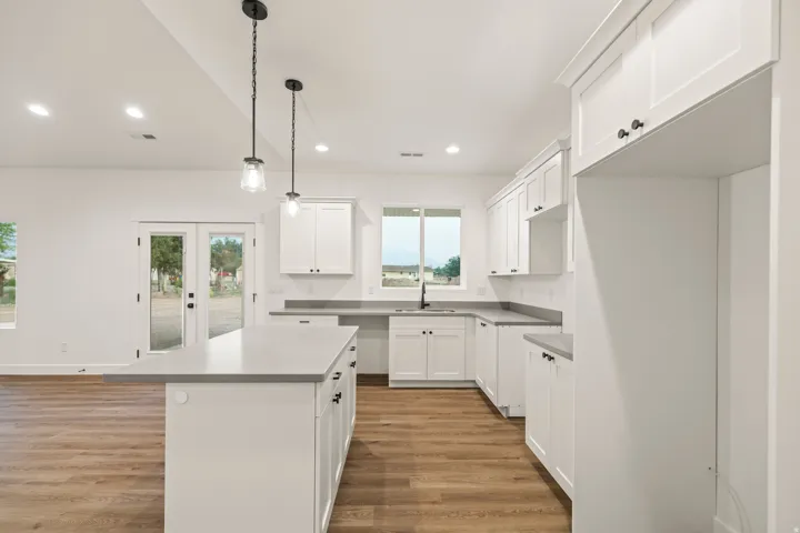 Modern kitchen featuring white shaker cabinetry, light-toned countertops, and wood-finish flooring