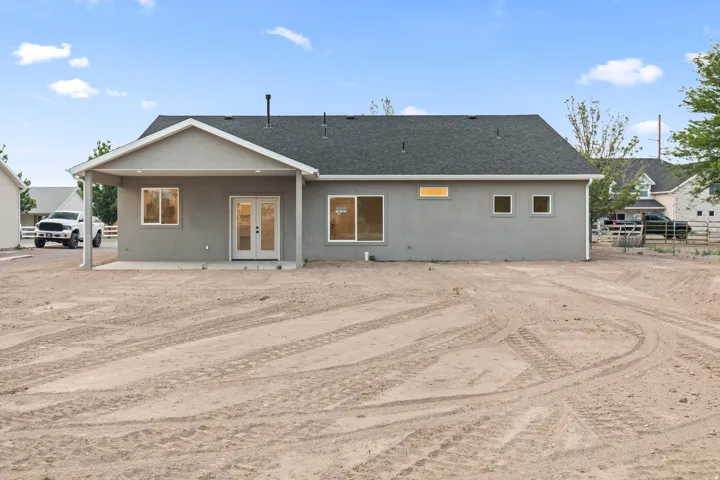 Rear exterior featuring a covered patio with concrete flooring, double French doors, multiple windows, and a dark shingle roof