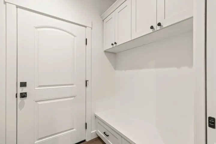 Entryway featuring an arched panel door with matte black hardware, built-in bench seating, upper cabinetry, and wood-finish flooring