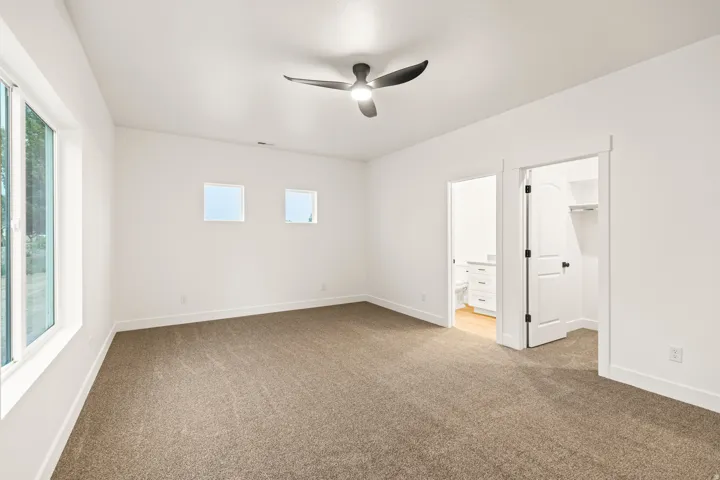 Spacious room featuring neutral carpet flooring, white walls, and a contemporary ceiling fan