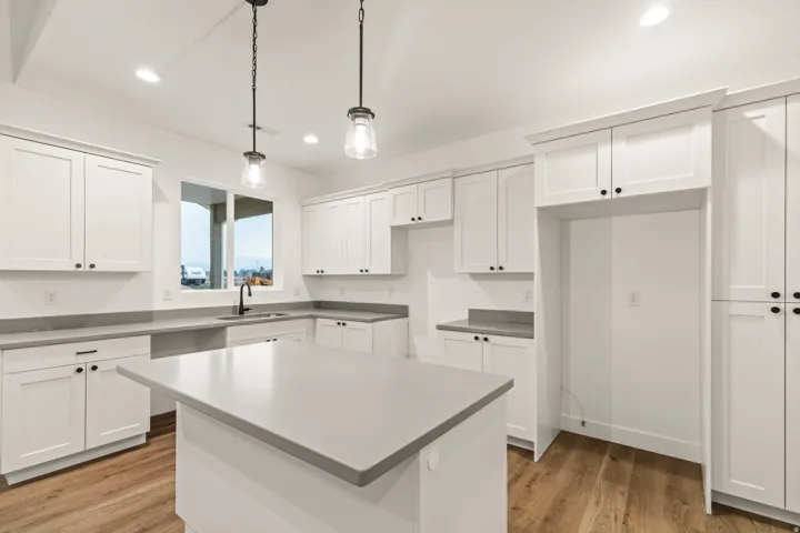 Kitchen featuring white shaker-style cabinetry, matte black hardware, light-toned countertops, a center island, and wood-finish flooring