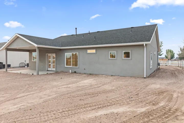 Rear exterior featuring stucco siding, a covered patio, a dark shingle roof, double patio doors, and multiple windows