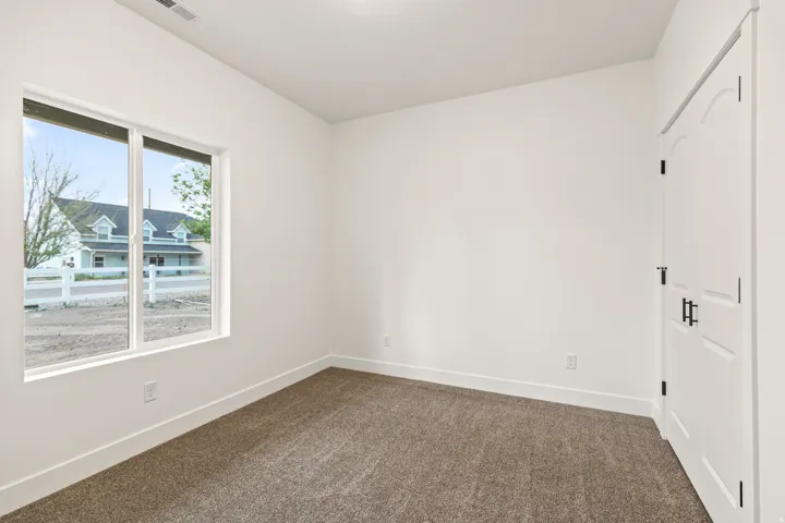 Room featuring a window with exterior views, carpeted flooring, white walls, and a white interior door with black hardware