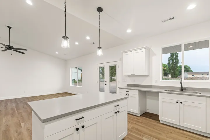 Open-concept kitchen featuring an island with white shaker cabinetry, light-toned countertops, and two pendant lights