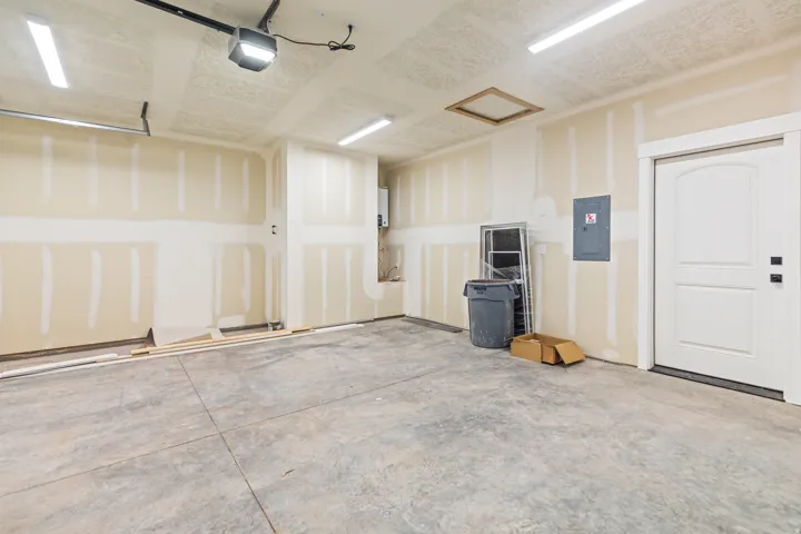 Spacious garage featuring a concrete floor, bright overhead lighting, and a white interior door