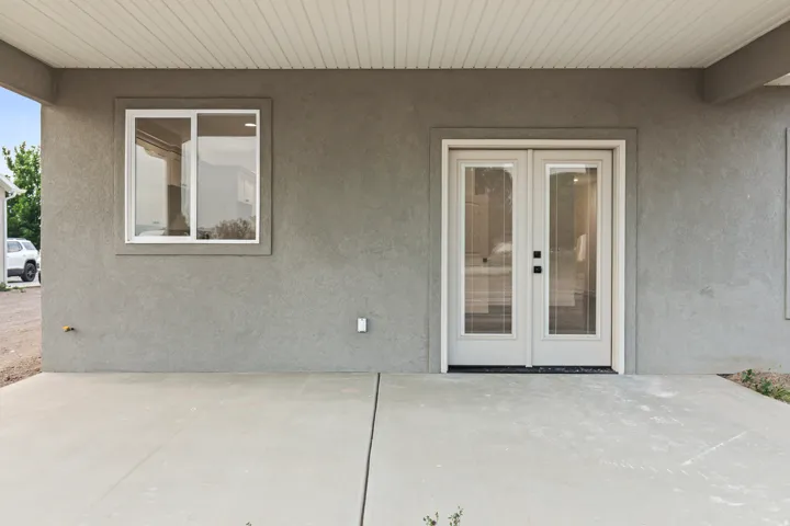 Covered concrete patio featuring textured stucco exterior, white frame sliding window, and double French doors with internal blinds