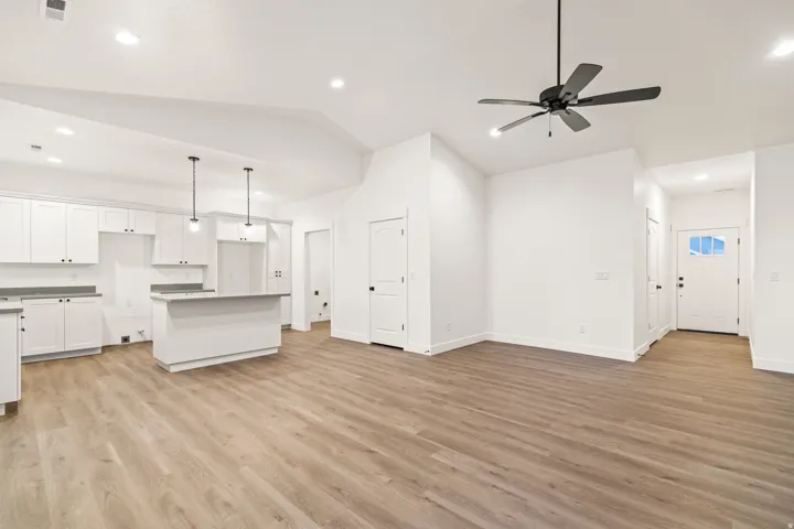 Open-concept living space featuring vaulted ceilings, wood-finish flooring, a modern kitchen island with pendant lighting, white cabinetry, and recessed lighting throughout