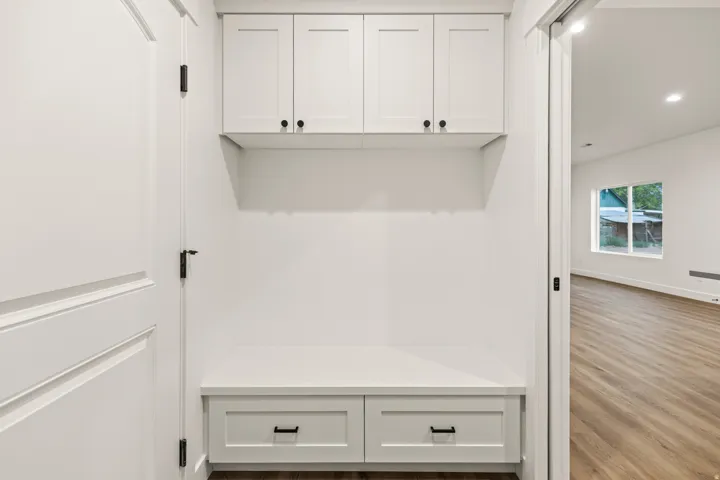 Built-in mudroom bench with two storage drawers, upper shaker-style cabinetry with matte black hardware, and wood-finish flooring