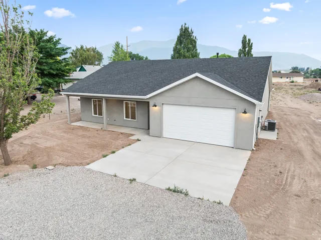 Contemporary stucco exterior featuring a two-car garage, covered entry, concrete driveway, dark shingle roof, and exterior lighting fixtures