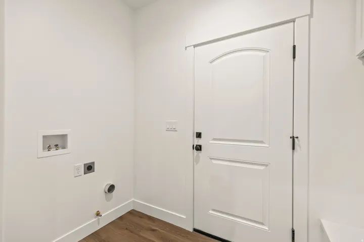 Dedicated utility area featuring wood-finish flooring, white walls, and a paneled door with dark hardware