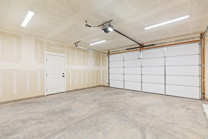 Spacious garage featuring a concrete floor, bright overhead strip lighting, white insulated garage door, and an interior access door