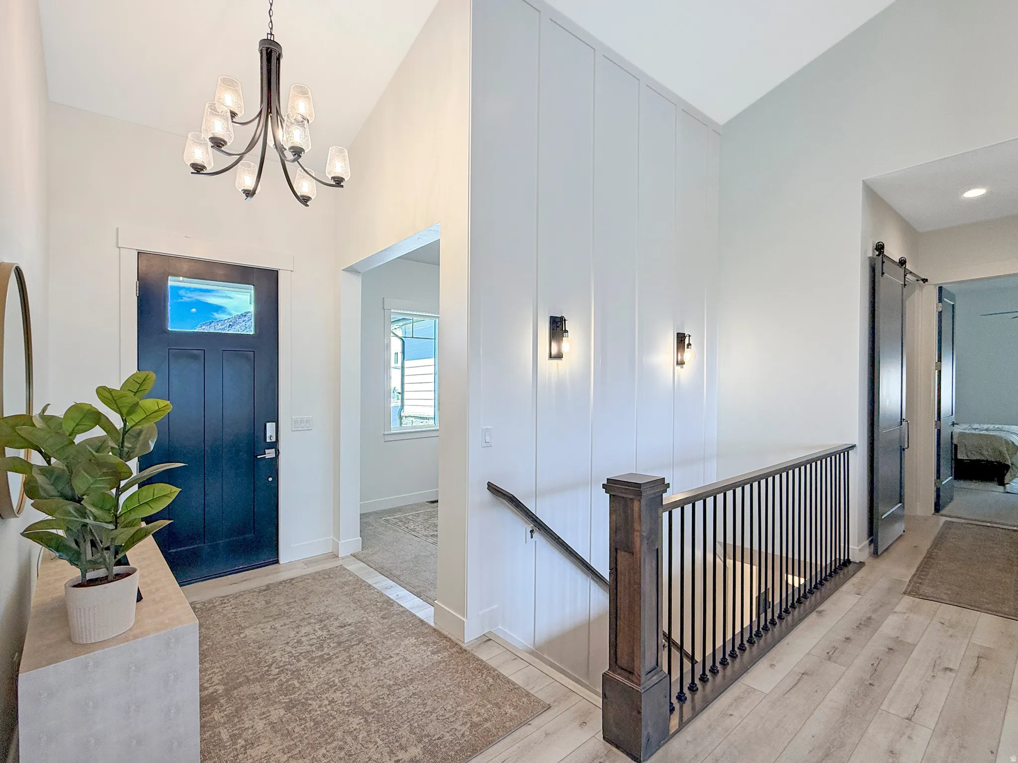 Light wood-finish flooring throughout, featuring a dark blue entry door with transom window and a contemporary chandelier