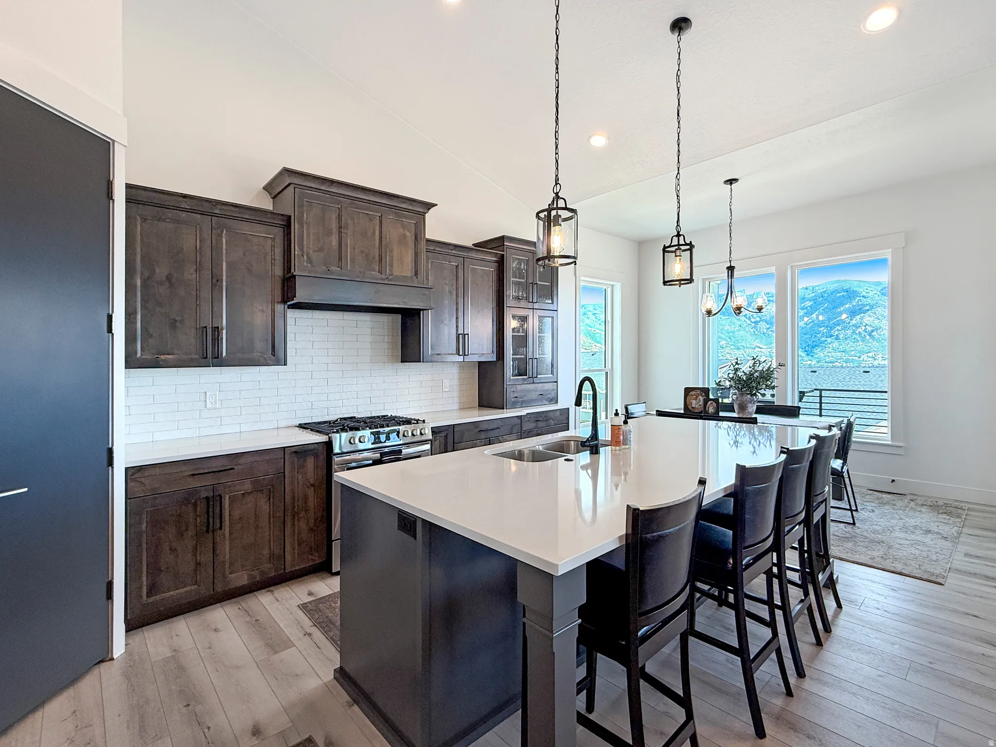 Modern kitchen featuring dark wood cabinetry, white subway tile backsplash, stainless steel range, and a large island with white countertops