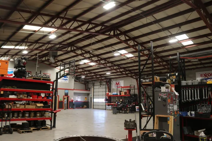 Spacious industrial interior featuring a high truss ceiling, multiple skylights, overhead lighting, a large roll-up door, and polished concrete flooring