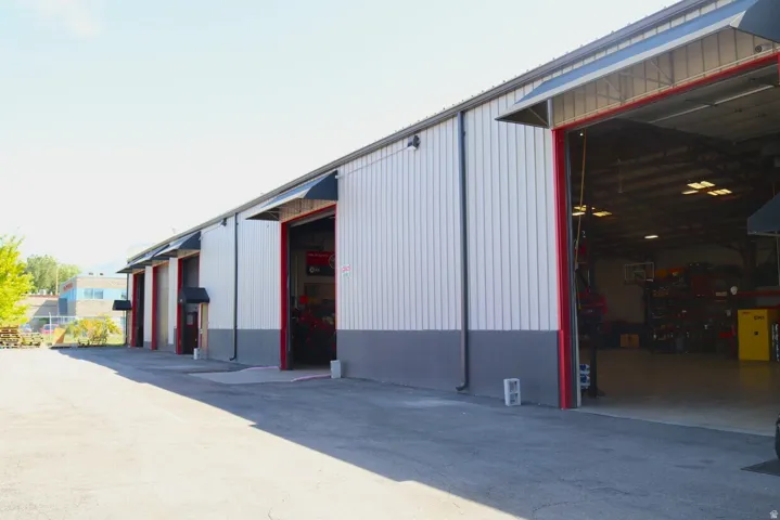 Industrial building exterior featuring multiple bay doors with red trim, corrugated metal siding in white and gray, and individual awnings