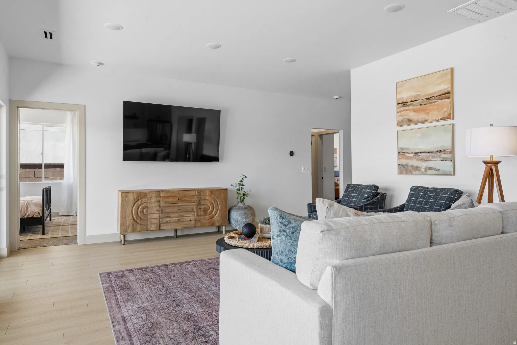Light wood-finish flooring extends through this living area, featuring recessed ceiling lights and a wall-mounted television above a wood console