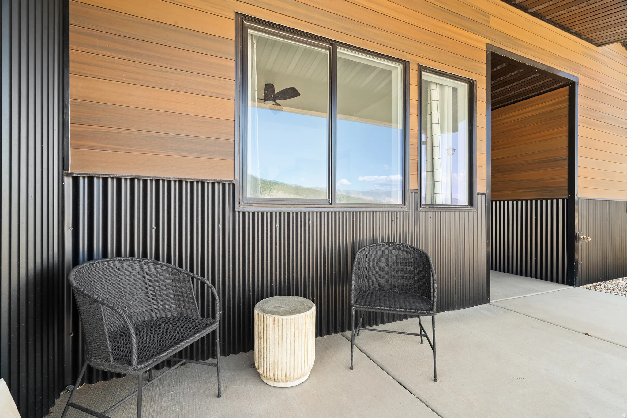 Exterior patio featuring wood-finish siding, corrugated metal accents, large windows with dark framing, and a concrete surface