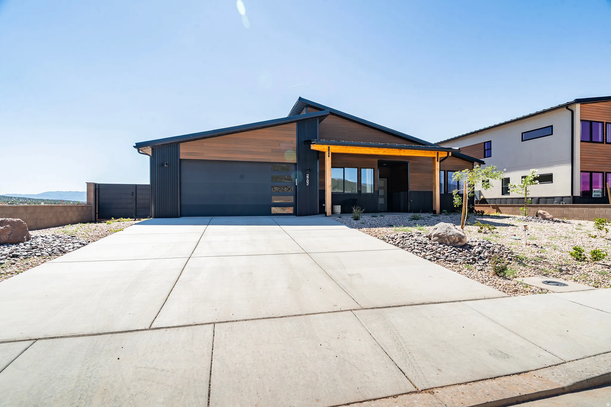 Modern exterior featuring dark vertical siding, wood-finish accent panels, and a prominent dark garage door with horizontal frosted glass inserts