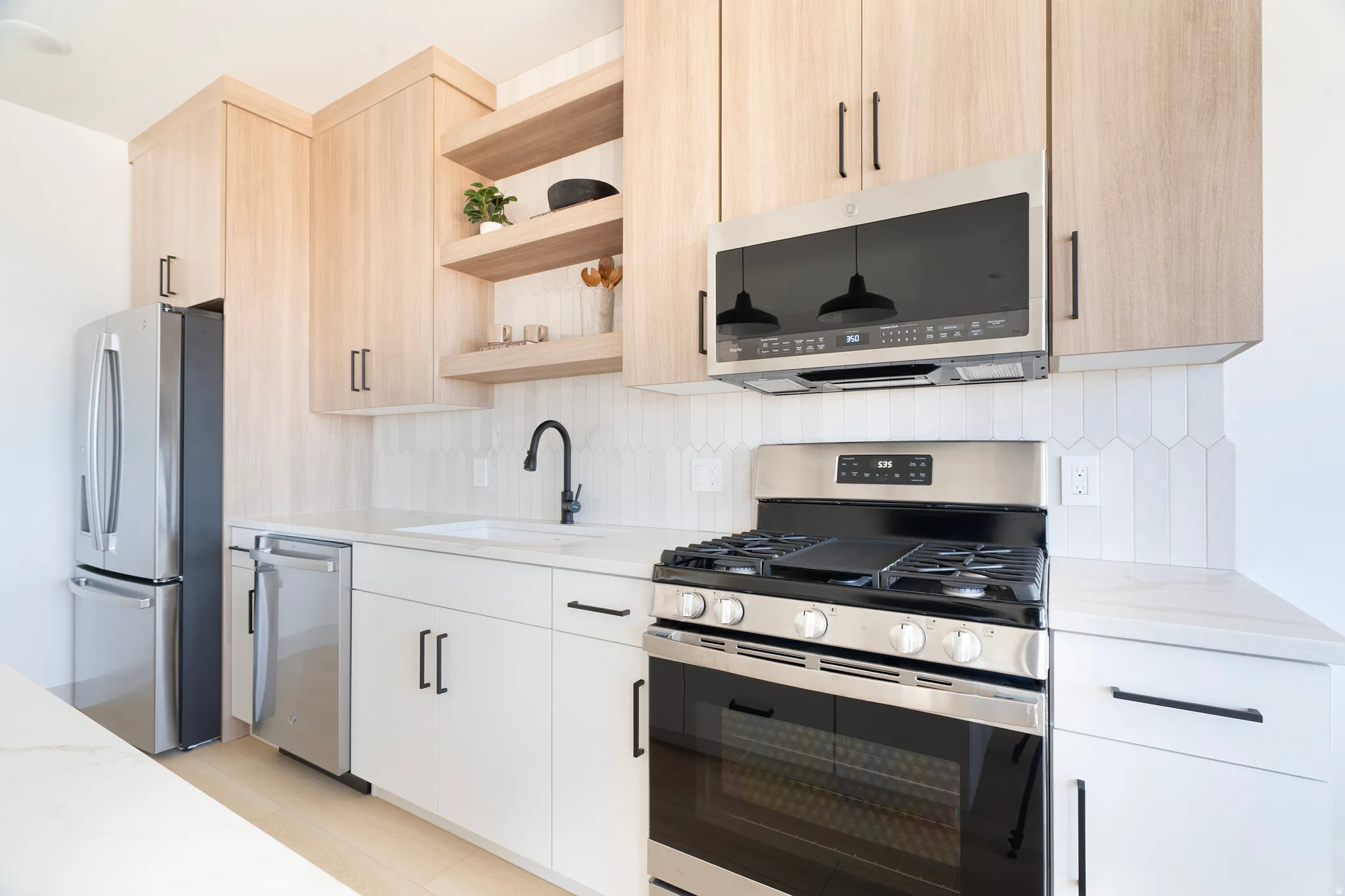 Modern kitchen featuring light wood-finish upper cabinetry, white lower cabinetry, and stainless steel appliances