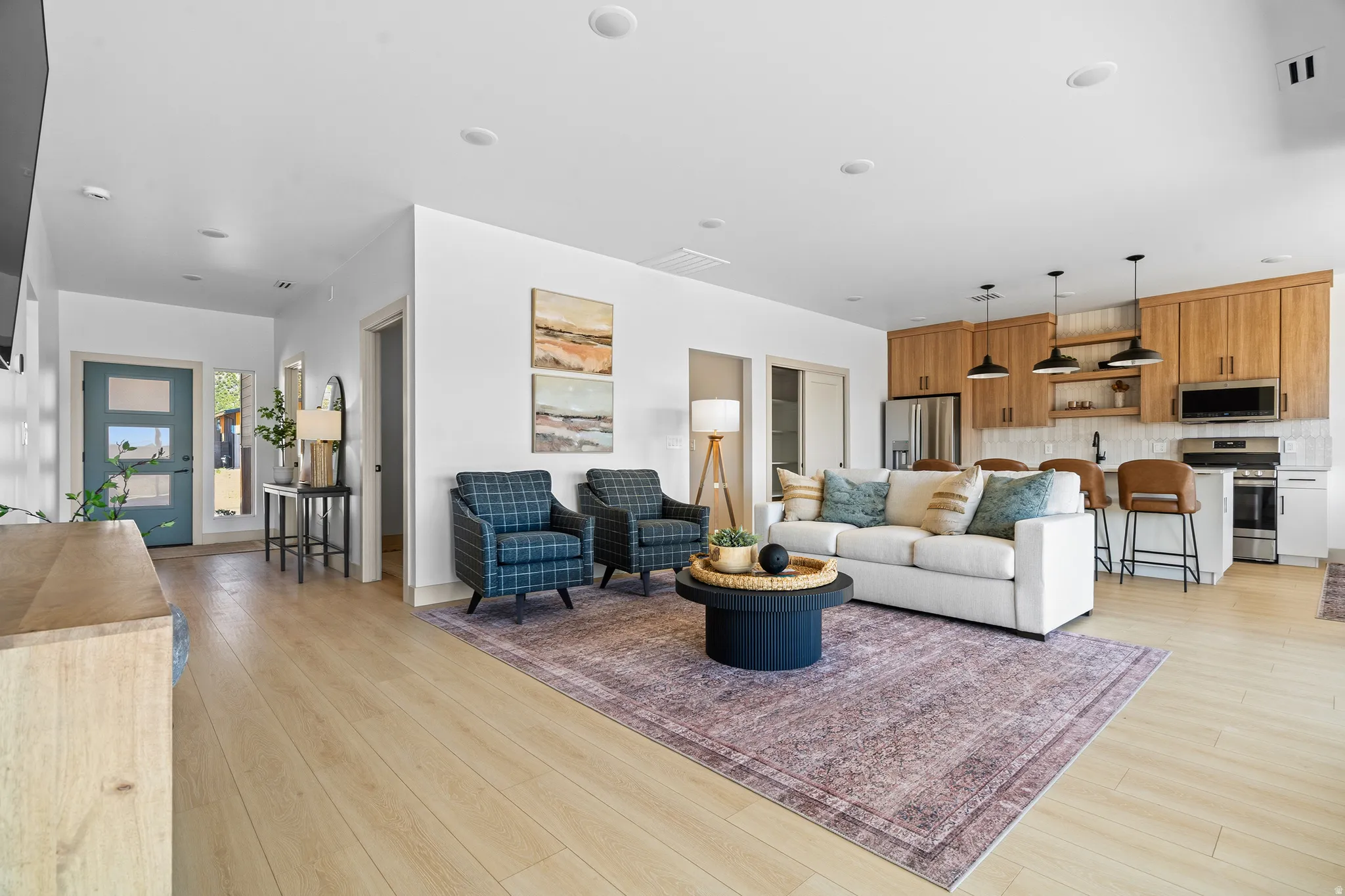 Open-concept living area with wood-finish flooring, recessed lighting, and a kitchen featuring wood cabinetry and stainless steel appliances
