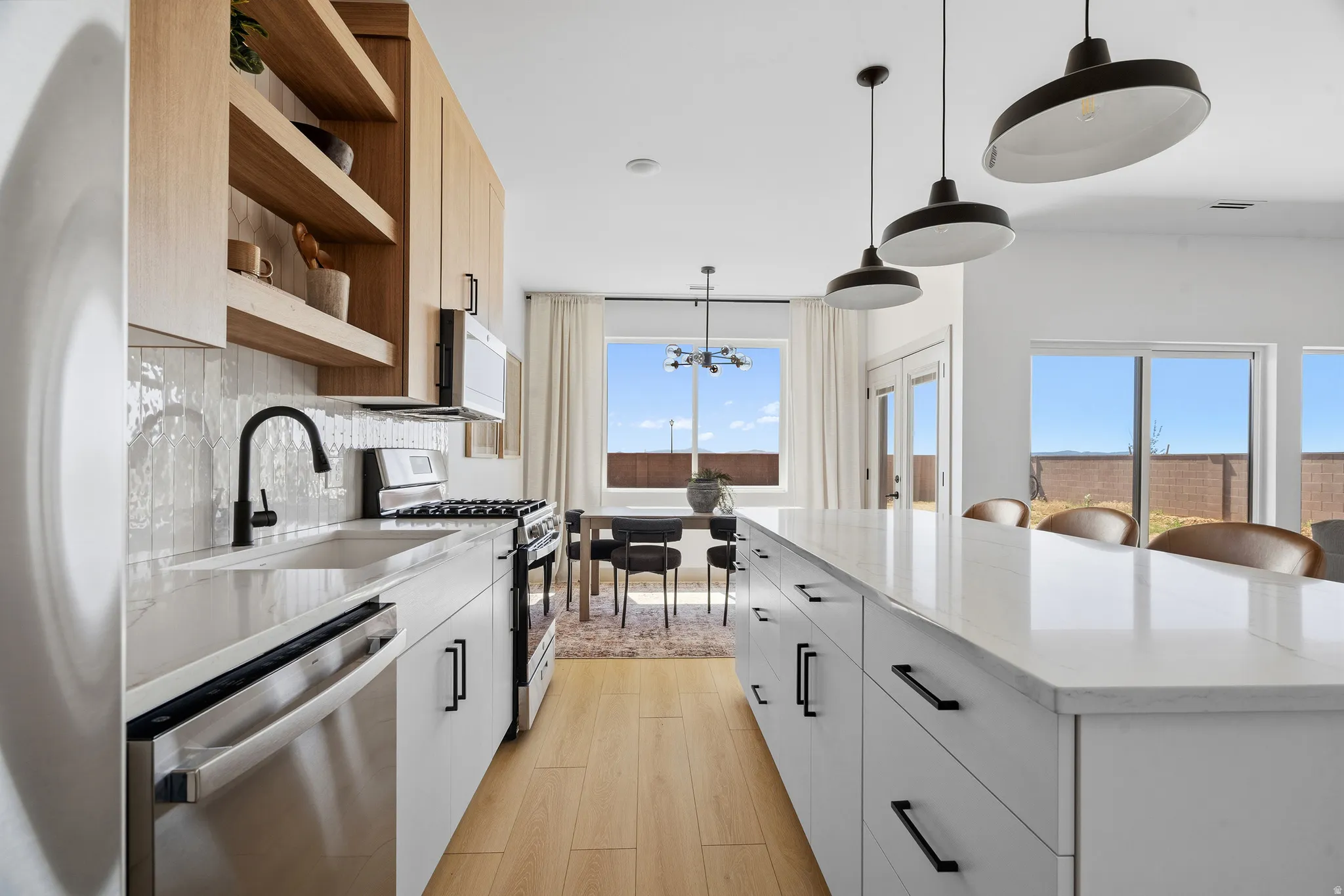 Contemporary kitchen with light wood-finish open shelving and cabinetry, white subway tile backsplash, stainless steel appliances, and a large central island featuring a white countertop