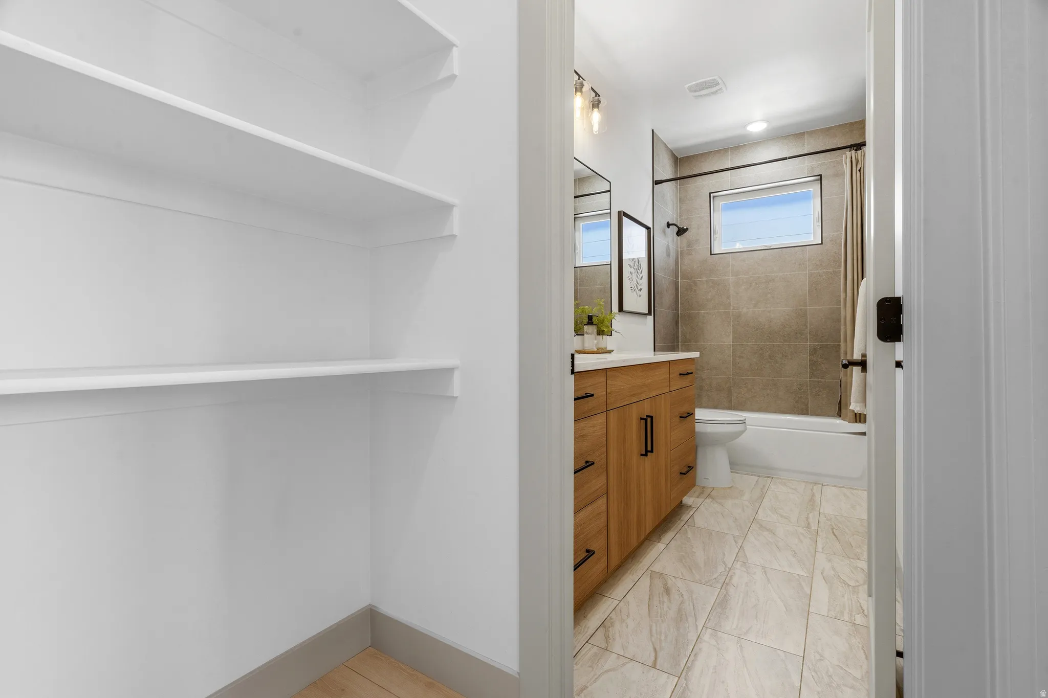 Bathroom featuring a wood-finish vanity with a light-colored countertop, a shower-over-tub combination with textured tile surround, and a coordinating tile floor