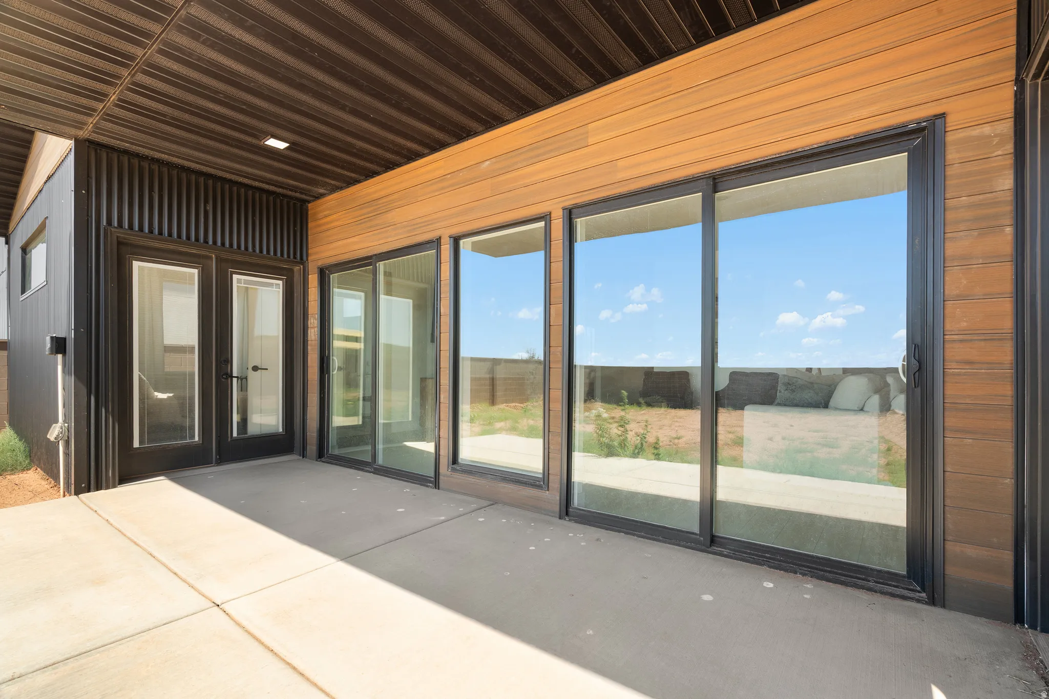 Covered concrete patio featuring multiple sliding glass doors and a double glass-panel door