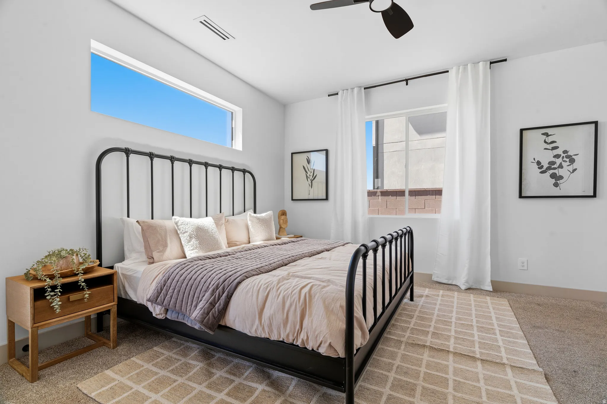 Bedroom featuring a wide transom window and an additional window with white curtains