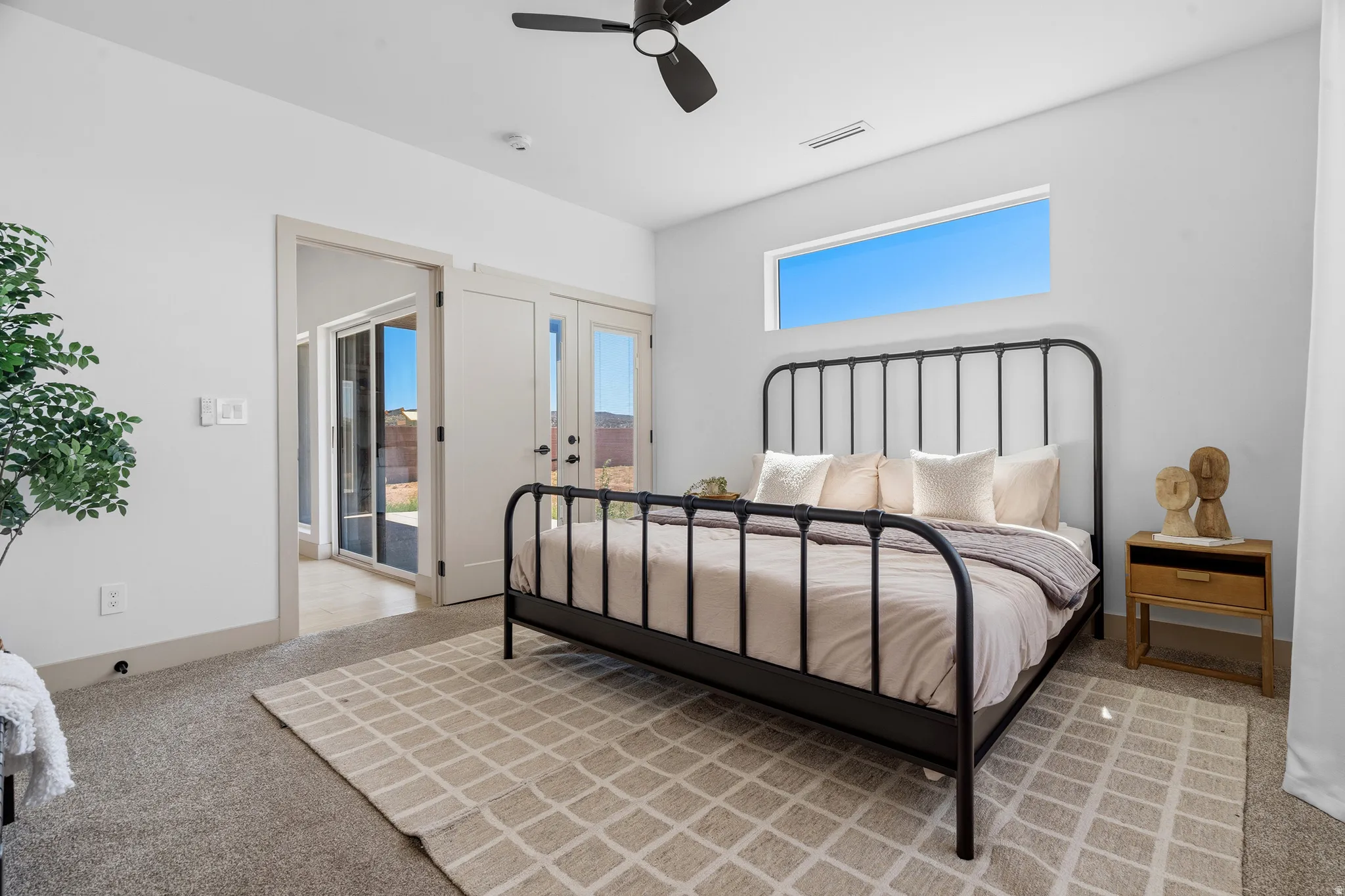 Carpeted room featuring a ceiling fan, transom window, and double French doors opening to an outdoor patio