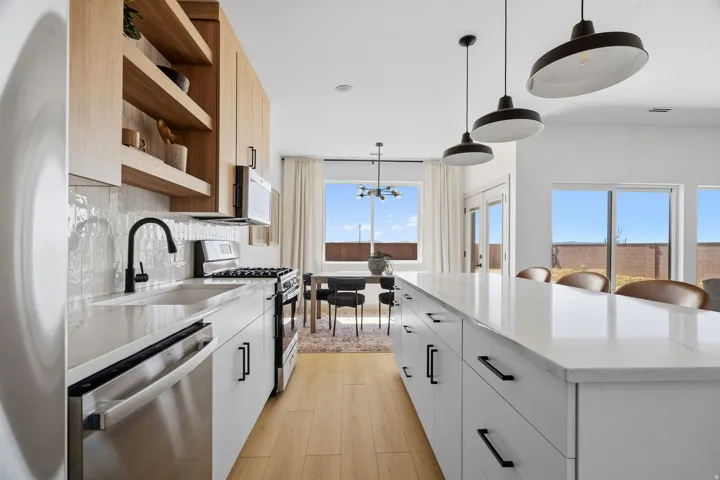 Contemporary kitchen with light wood-finish open shelving and cabinetry, white subway tile backsplash, stainless steel appliances, and a large central island featuring a white countertop
