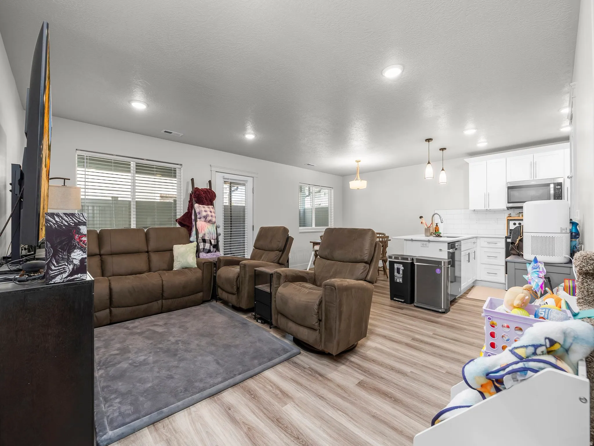 Open-concept living space featuring wood-finish flooring throughout, white walls, and recessed lighting