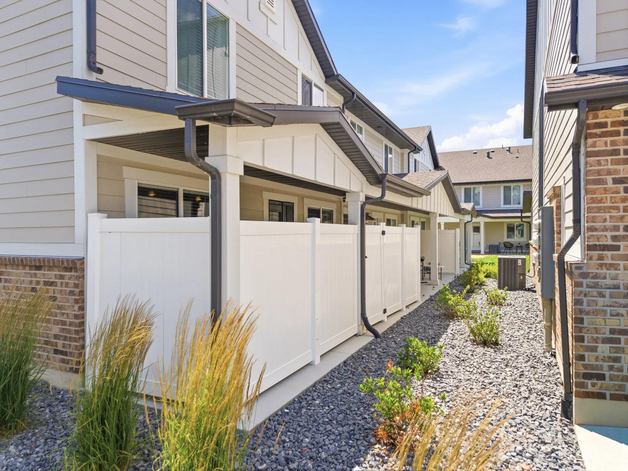 Exterior featuring a covered patio, white privacy fencing, and a landscaping bed with decorative rock and low-maintenance plantings