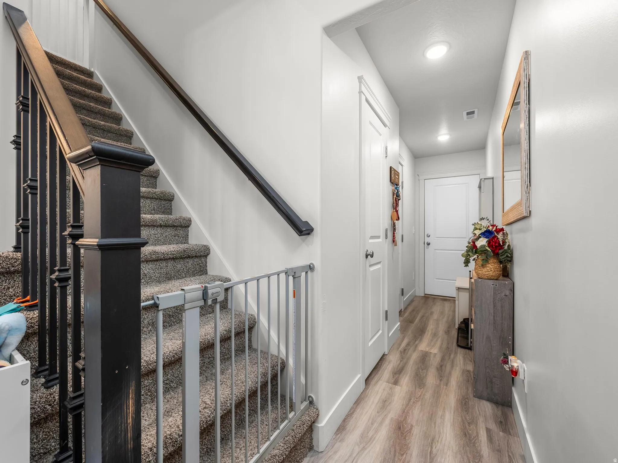 Carpeted staircase with dark wood newel post and balusters, featuring a light wood-finish flooring hallway with white walls, recessed lighting, and white paneled doors
